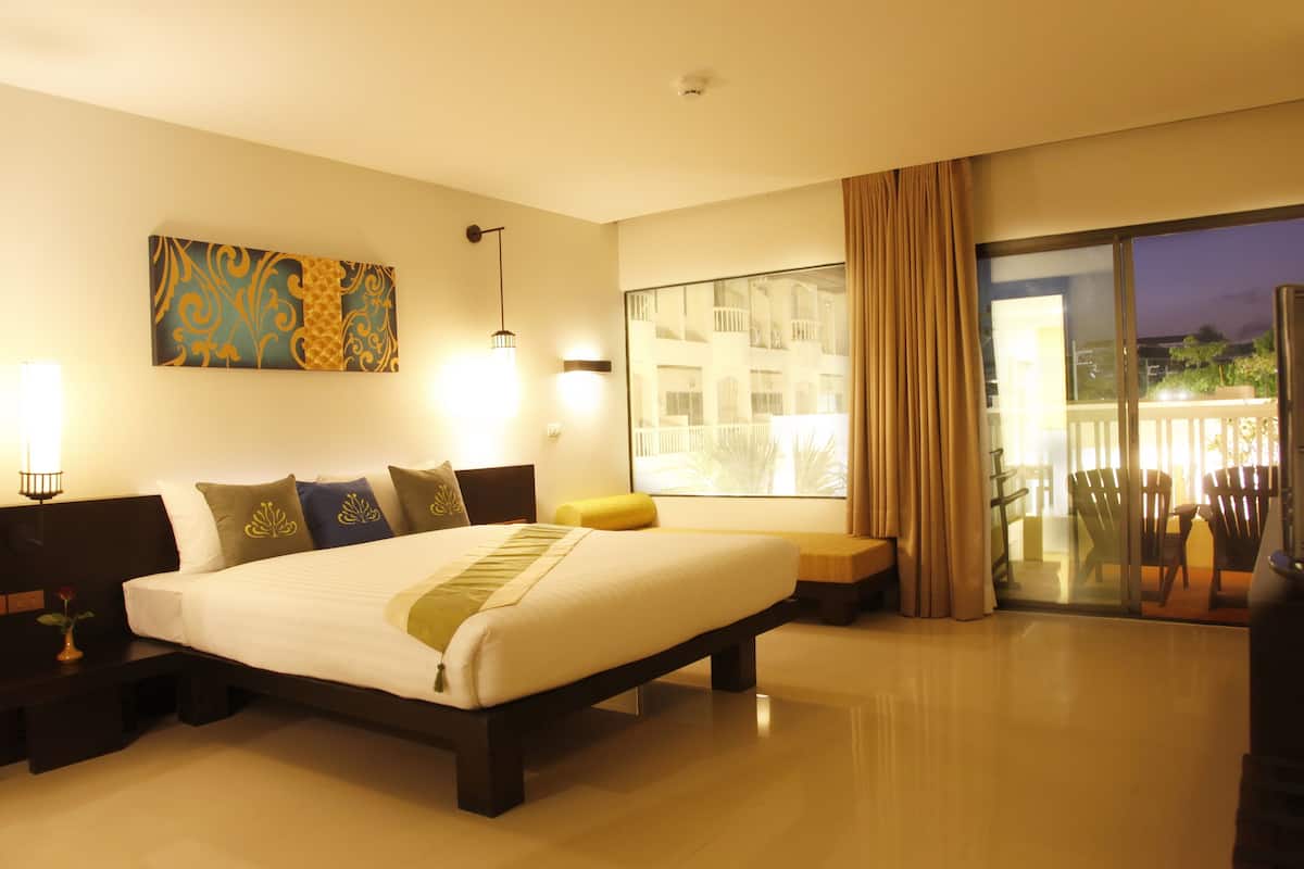 A hotel room with a large bed, bedside lamps, a painting on the wall, and a balcony with chairs.