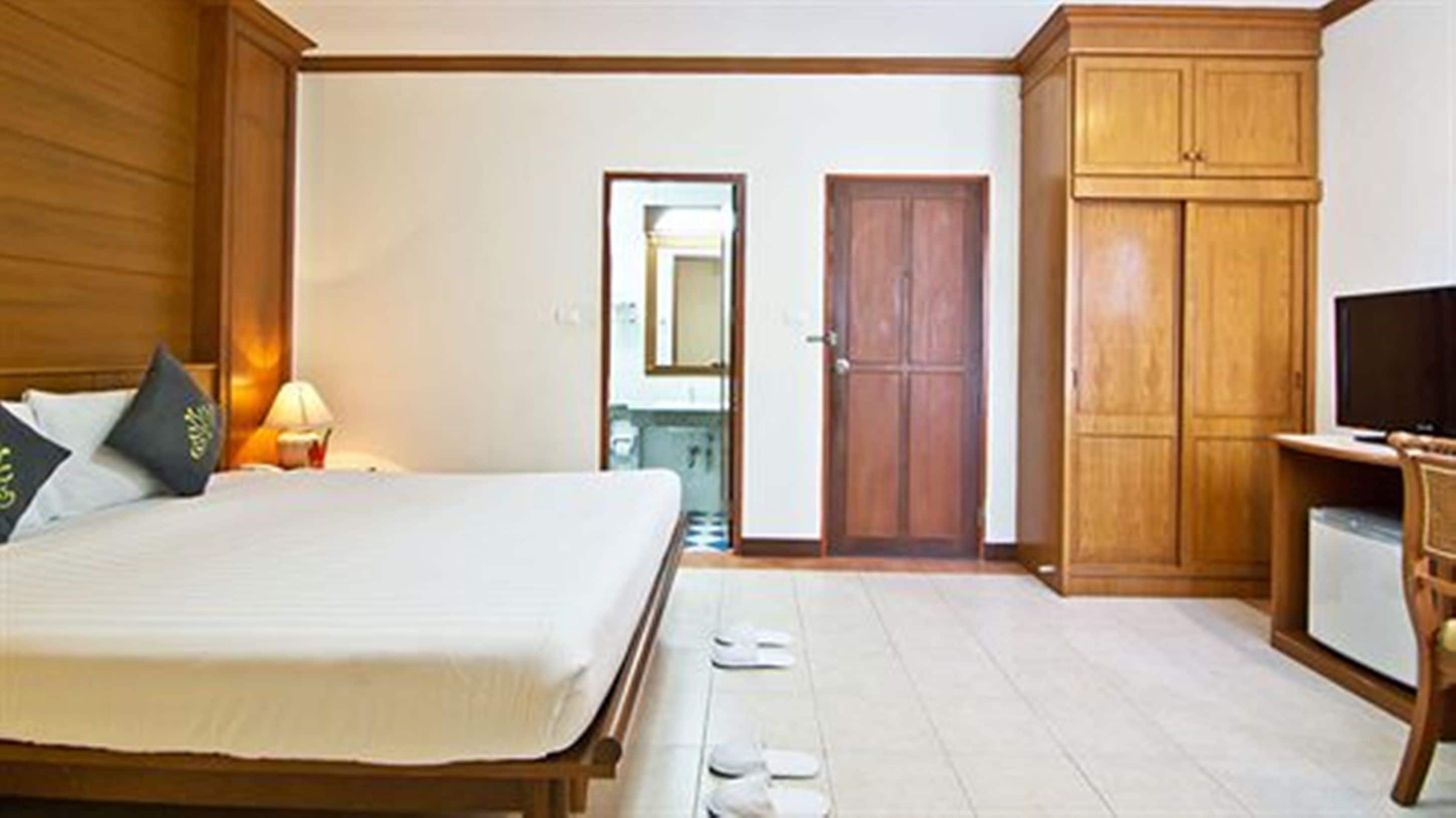 A bedroom with a bed, a television, a wardrobe, and a bathroom visible through an open door.