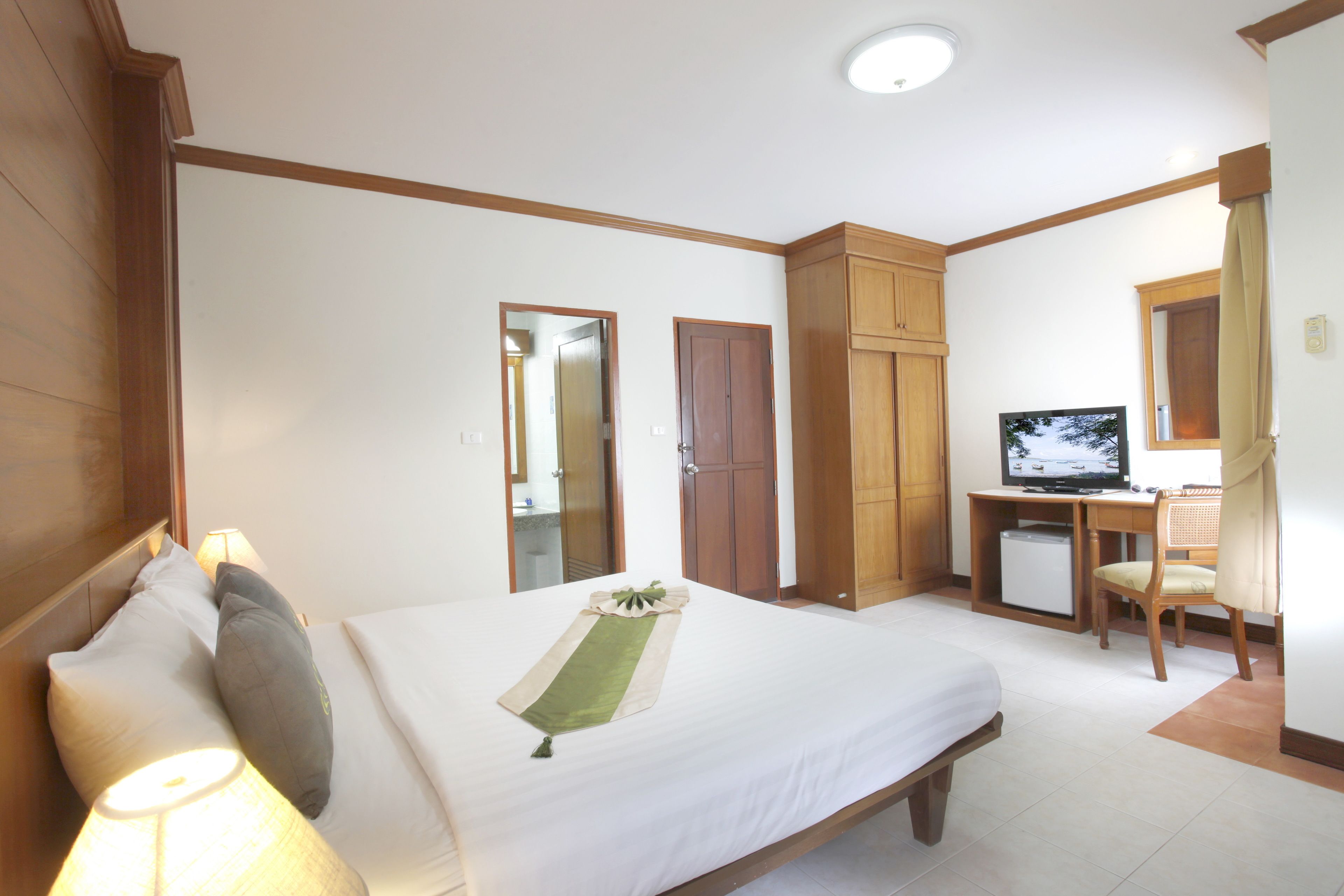 A hotel room with a bed, a desk with a television, a chair, and a wardrobe.