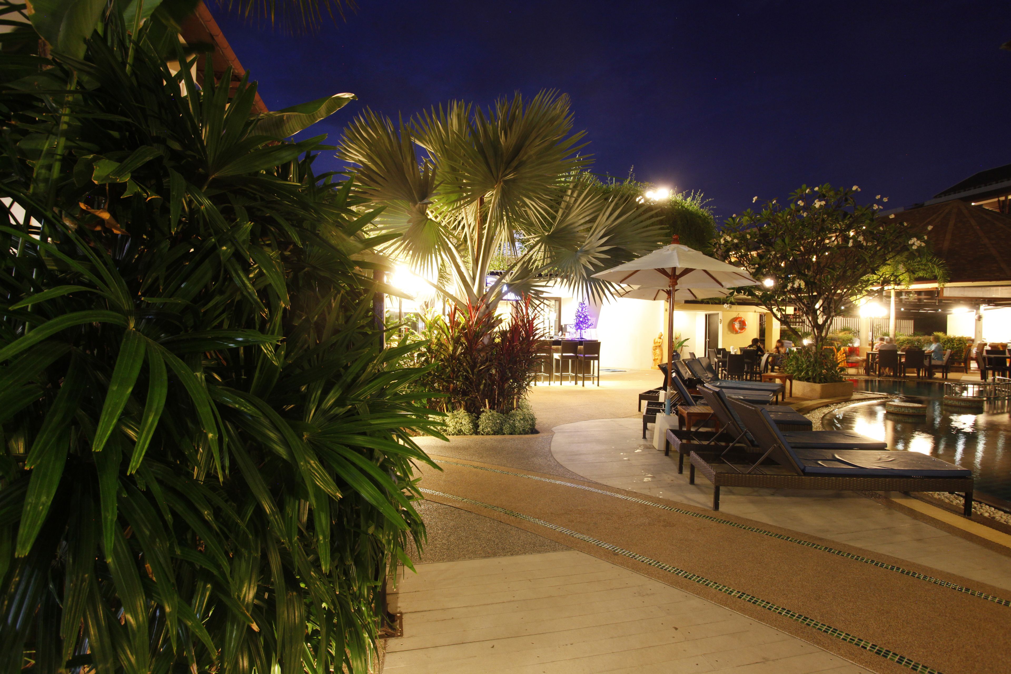 A poolside area with lounge chairs and umbrellas, surrounded by lush greenery.