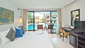 A hotel room with a bed, a desk, a TV, and a view of an outdoor swimming pool.