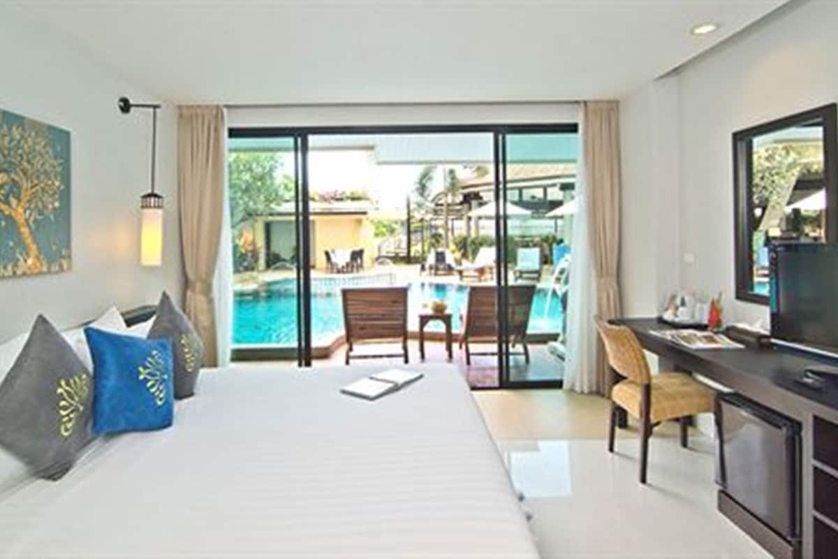 A hotel room with a bed, a desk, a TV, and a view of an outdoor swimming pool.