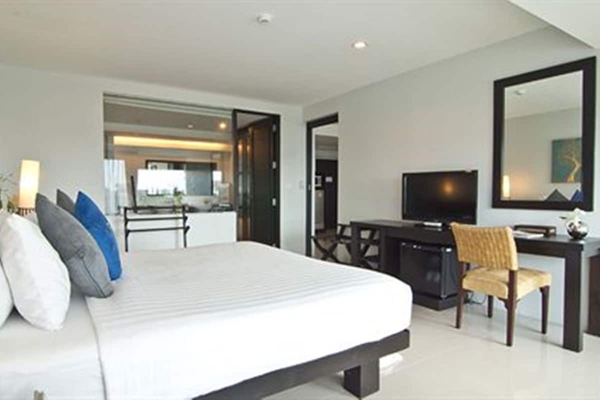 A modern hotel room with a large bed, a desk with a chair, a television, and a mirror.