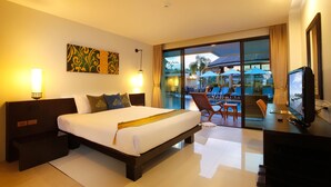 A hotel room with a large bed, a desk with a computer, a TV, and a view of the outdoor pool area.