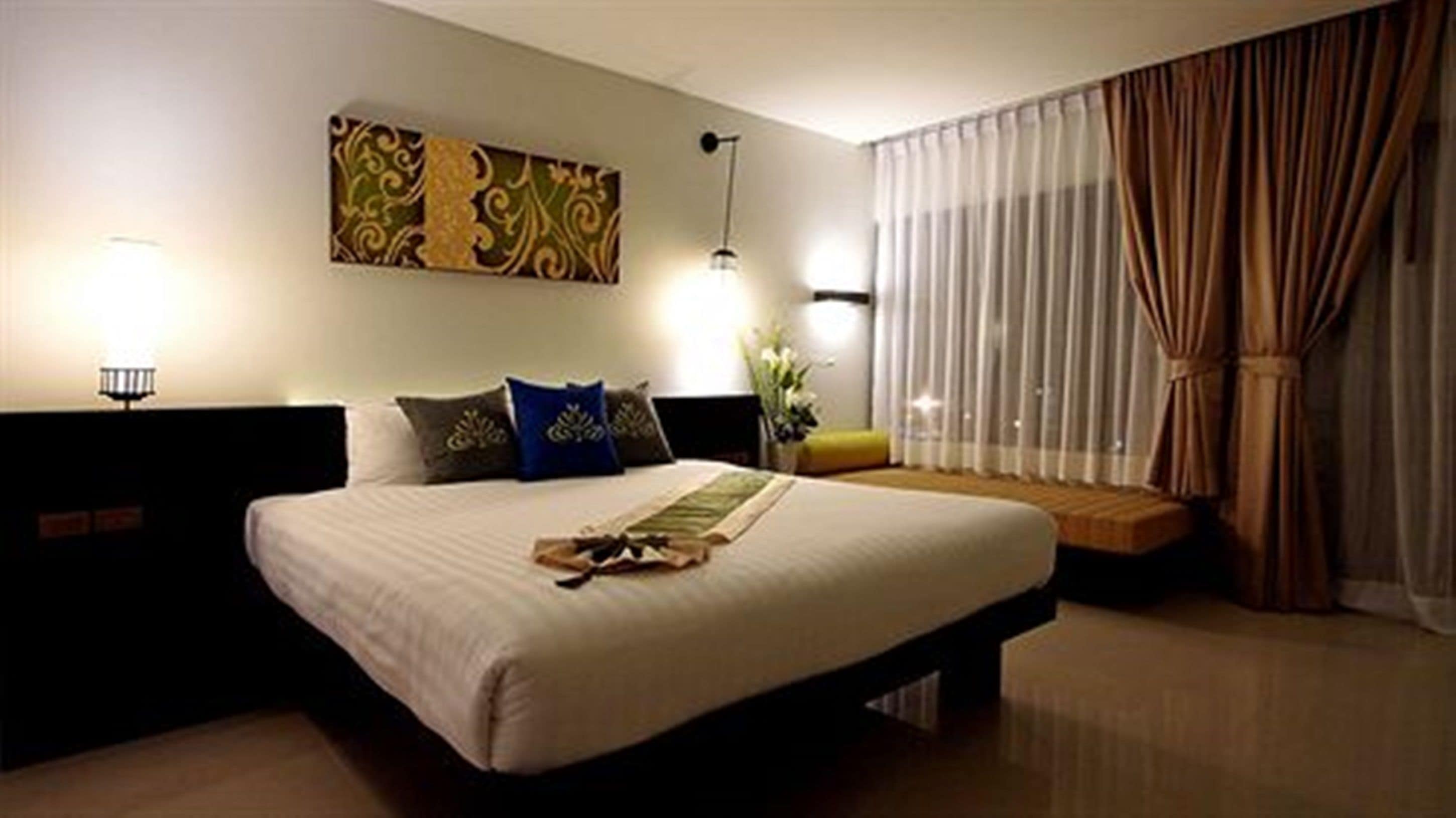 A hotel room with a large bed, a nightstand, a lamp, and a window with curtains.