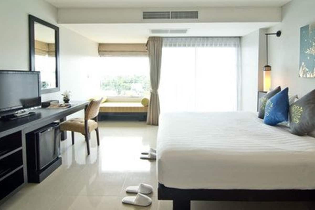A hotel room with a bed, a desk with a TV, a chair, slippers, and a window with curtains.