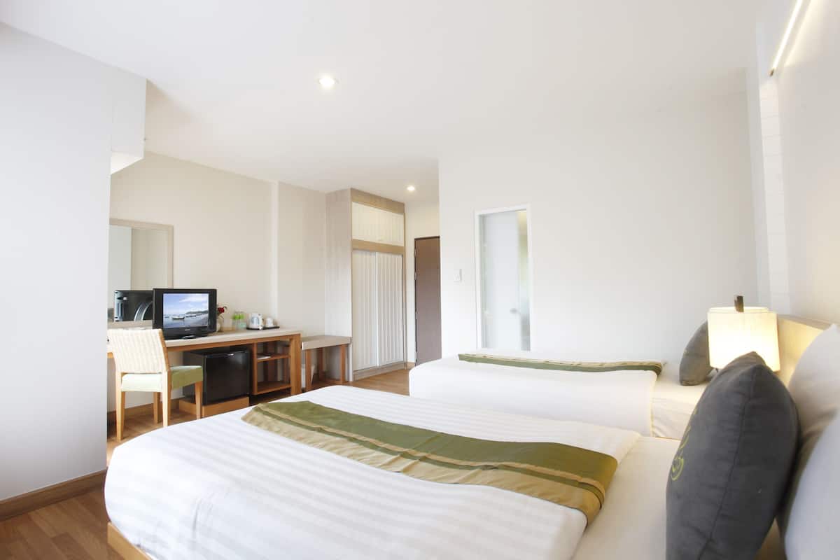 A hotel room with a bed, a desk with a television, a chair, and a lamp.