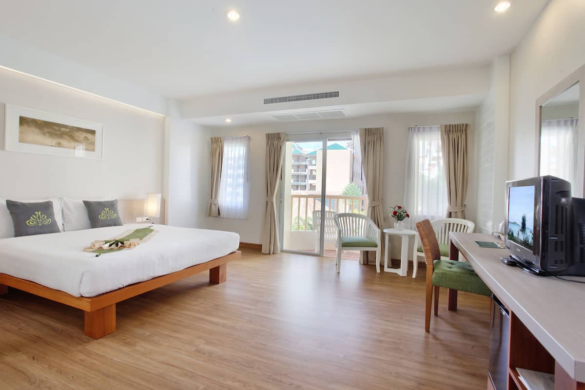 A hotel room with a bed, a TV, a desk, and a balcony with a view of buildings.