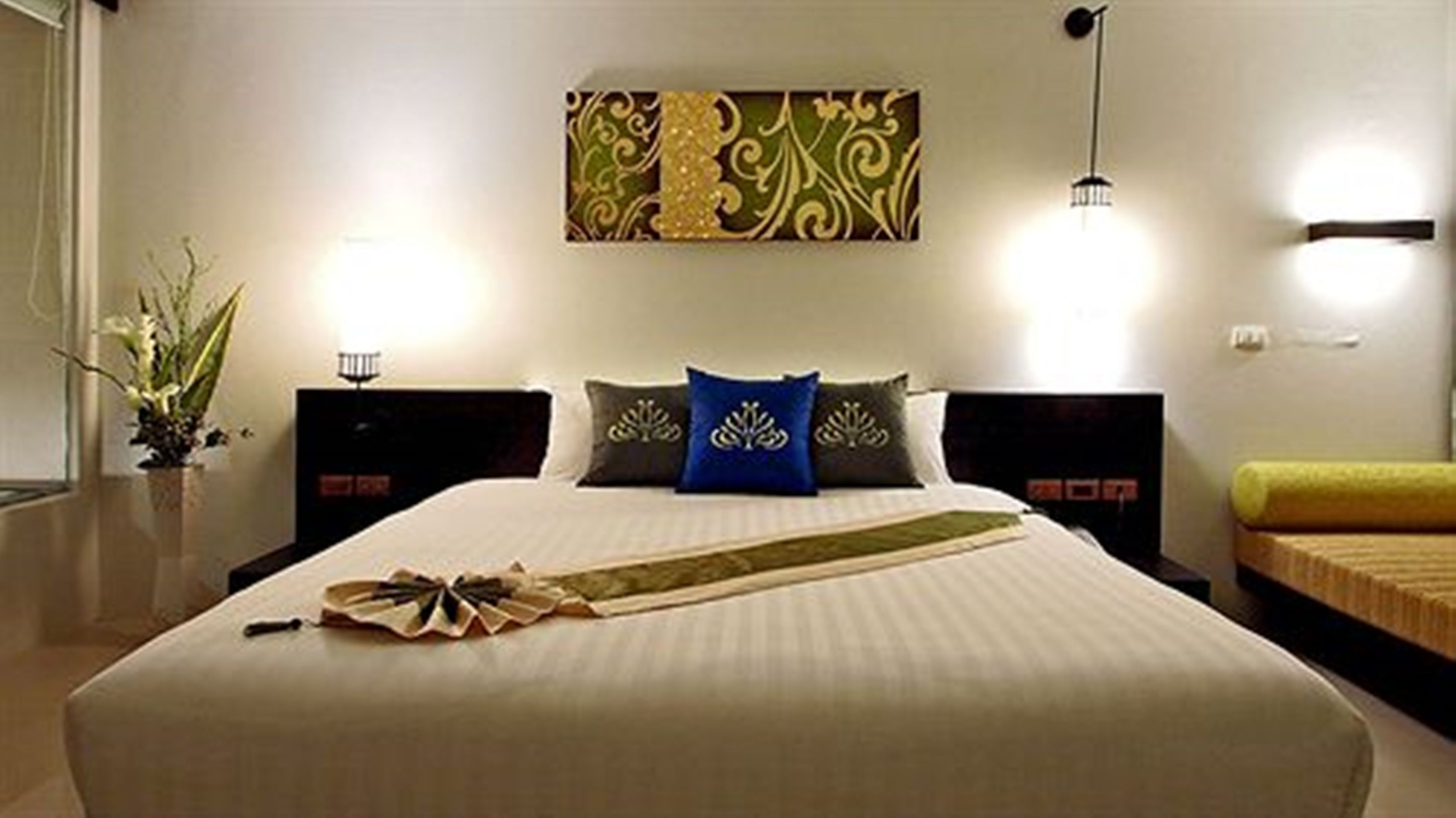 A neatly made bed with a decorative headboard, a bedside table with a lamp, and a wall-mounted artwork.