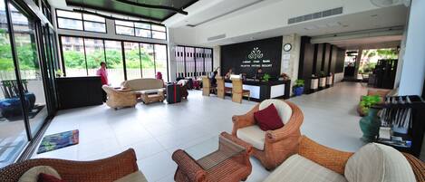 A spacious lobby with wicker furniture, a reception desk, and large windows offering views of greenery.