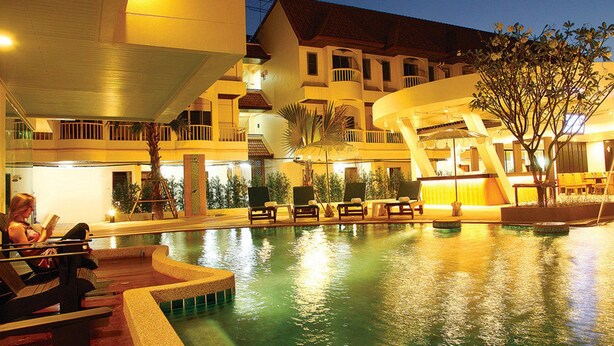 A pool area with lounge chairs and umbrellas, surrounded by buildings with balconies and outdoor seating.