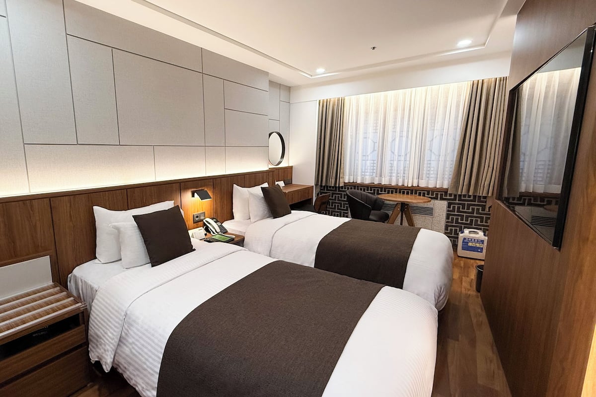 A hotel room with two beds, a desk, a chair, a small table, and a mirror.