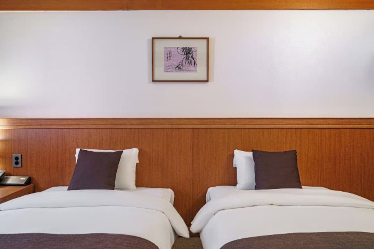 A hotel room with two beds, a wooden headboard, a framed picture on the wall, and a bedside table with a lamp.