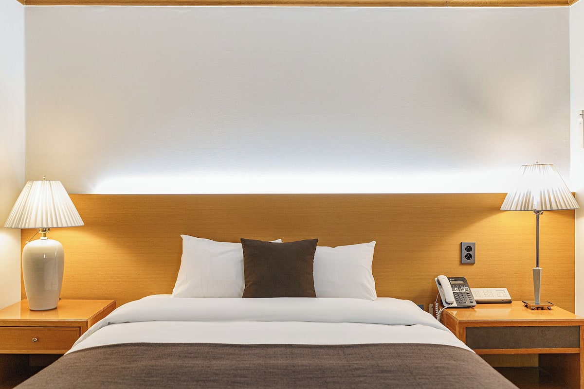 A neatly made bed with white and brown bedding, two bedside lamps, and a telephone on the nightstand.
