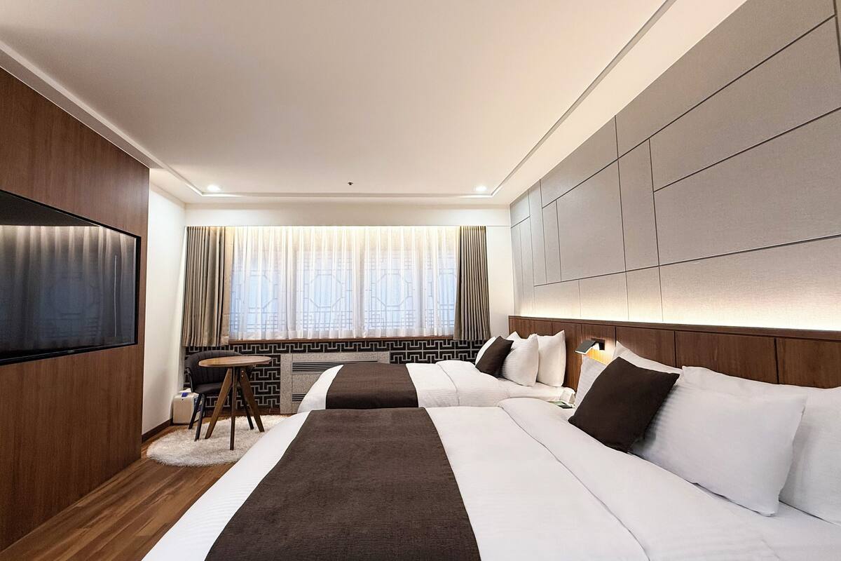 A modern hotel room with a large bed, a flat-screen TV mounted on the wall, and a small table with a chair.
