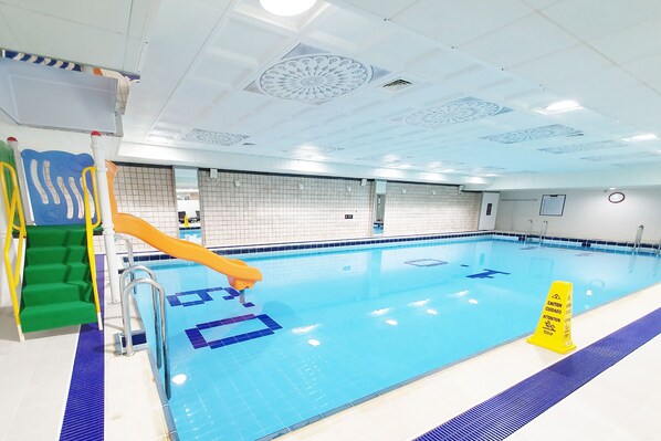 Una piscina con un letrero de precaución, un tobogán y una escalera.