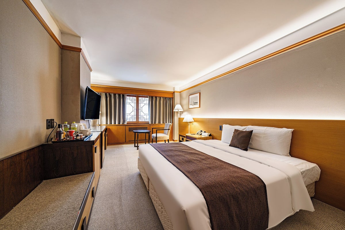 A hotel room with a large bed, a desk with a chair, a TV, and a window with curtains.