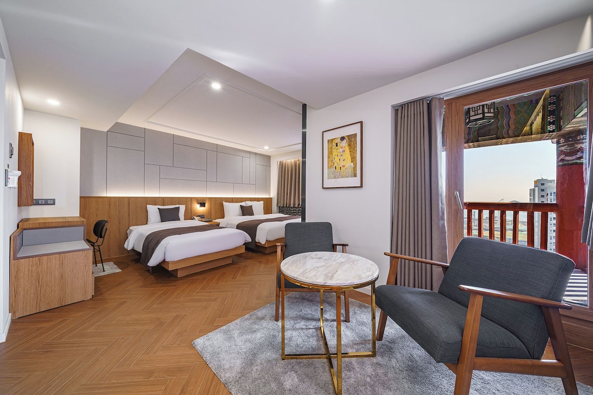 A modern hotel room with a large bed, two smaller beds, a round table, and a balcony with a view.