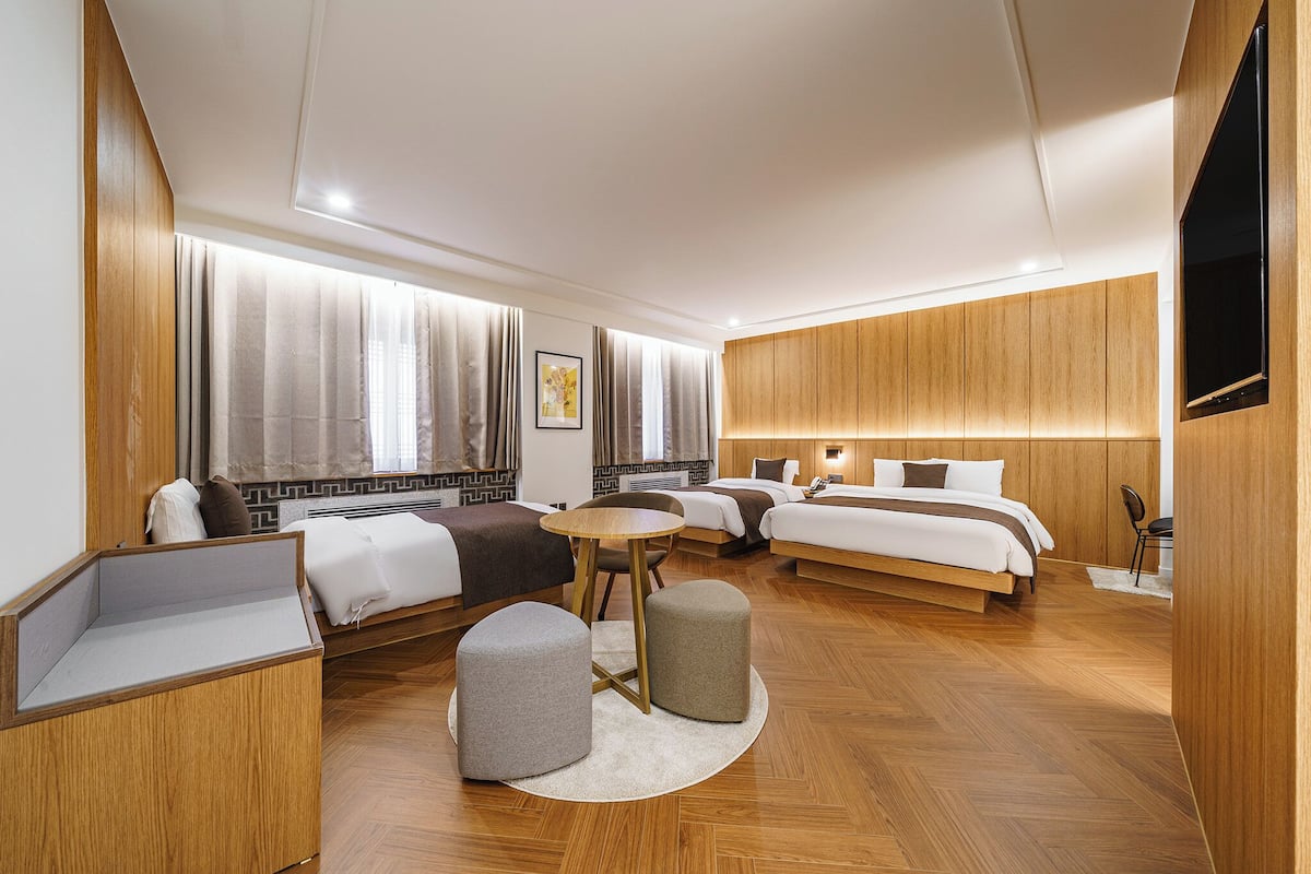A modern hotel room with two beds, a sofa, a small table, and a TV.