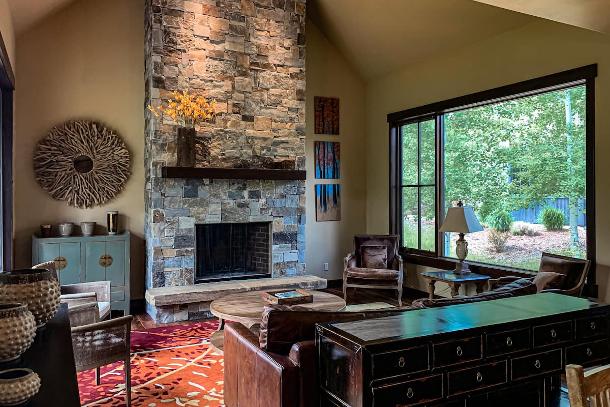 A living room with a stone fireplace, a large window, and a view of the outdoors.