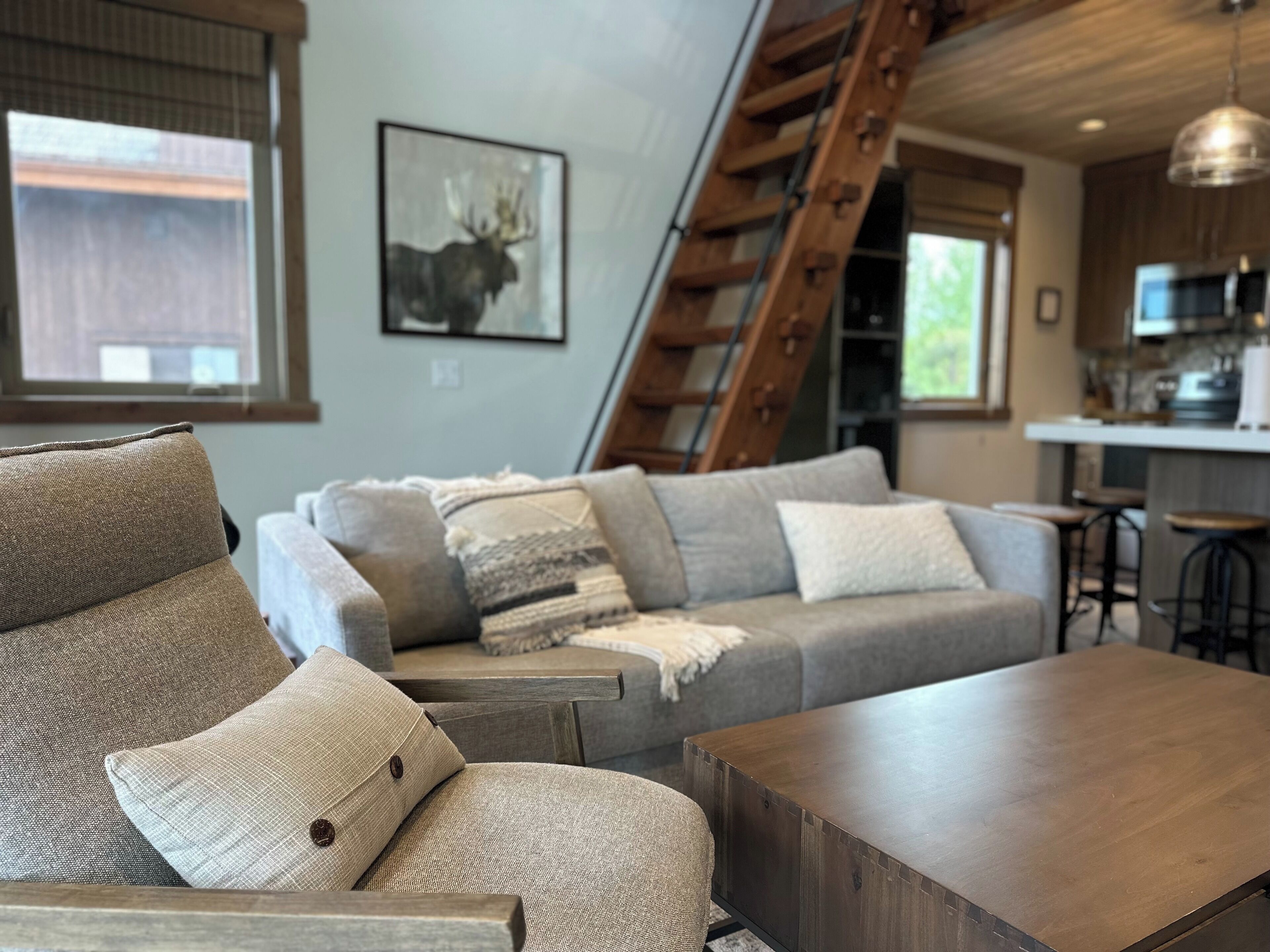 A modern living room with a sofa, a wooden coffee table, and a ladder leading to a kitchen area.