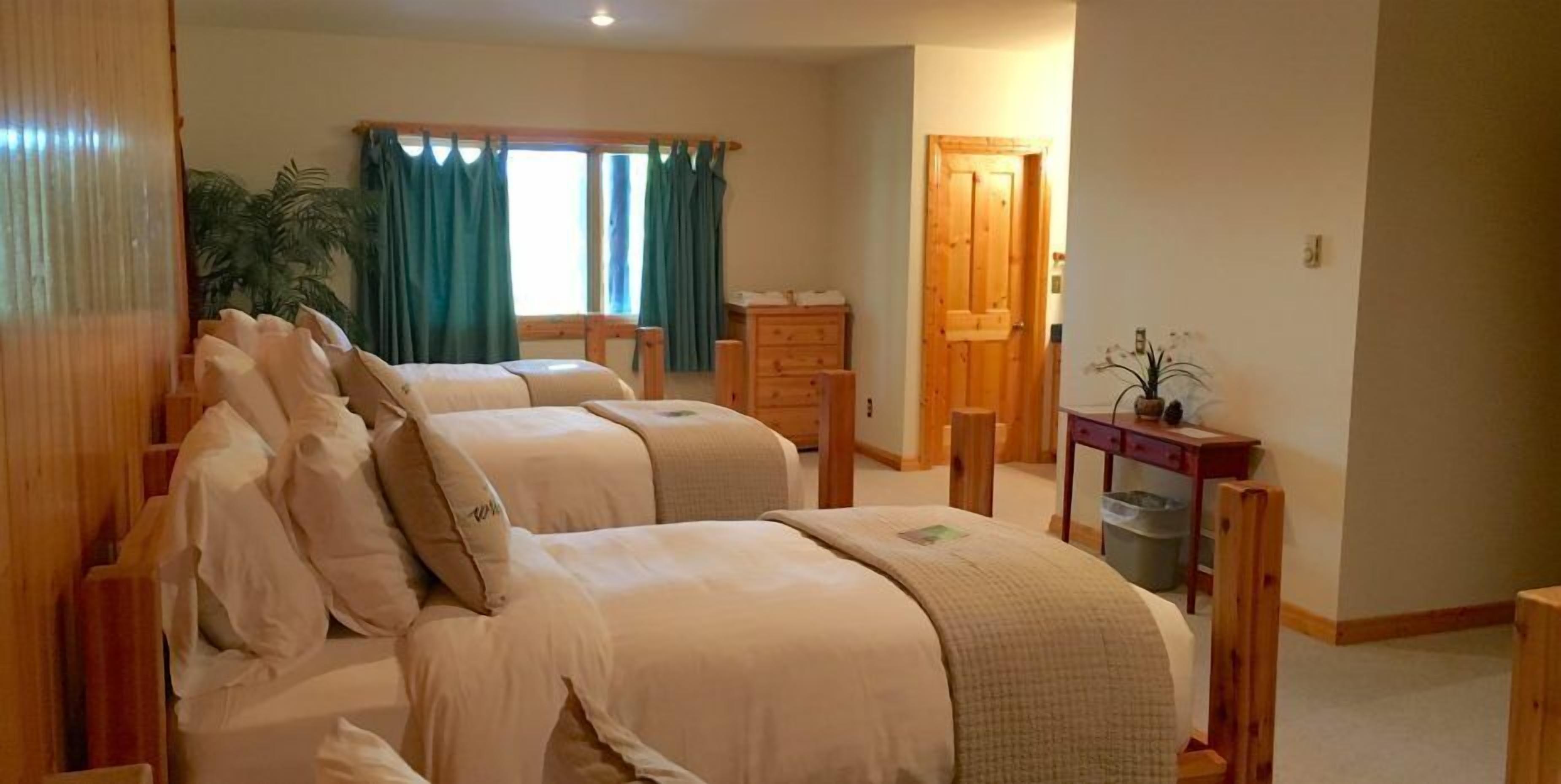 Un dormitorio con dos camas, un escritorio de madera, una silla, un aparador y una ventana con cortinas.