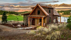 A rustic cabin with a wooden exterior, a porch with chairs, and a view of mountains and a lake. - Wilderness Club (Eureka)