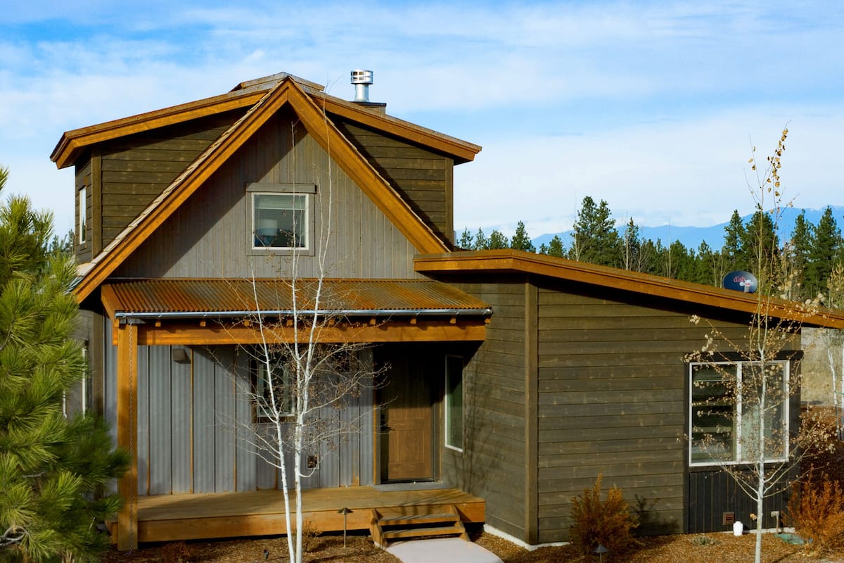 A two-story wooden house with a sloped roof, a front porch, and a small window.