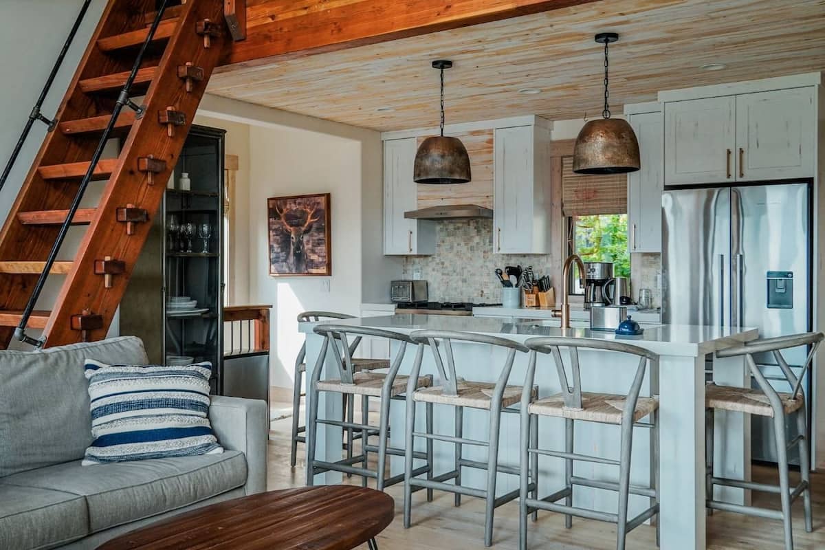 A modern kitchen with a central island, bar stools, and a staircase leading to another level.