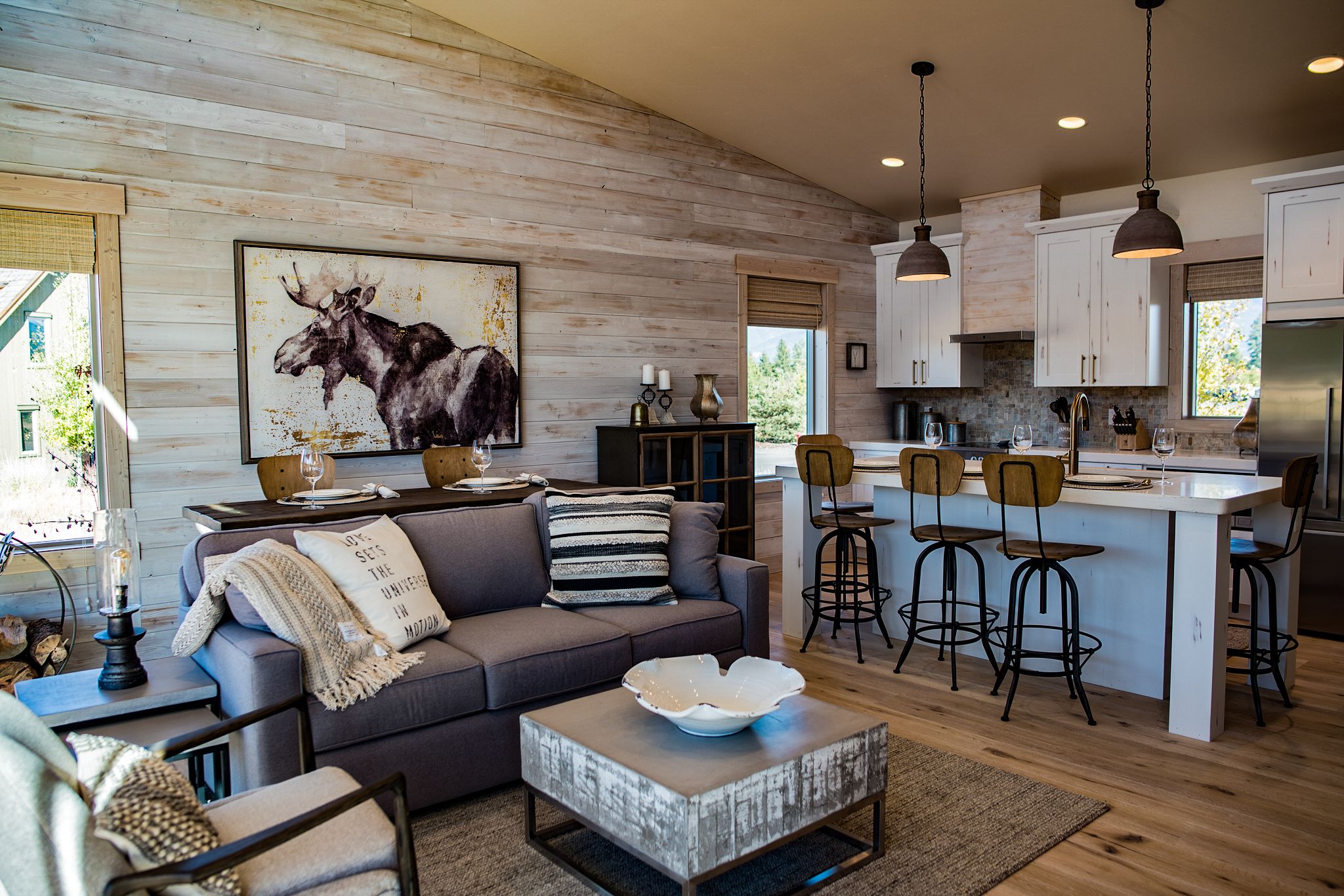 A modern kitchen with wooden cabinets, a dining area with bar stools, and a living room with a sofa and a coffee table.