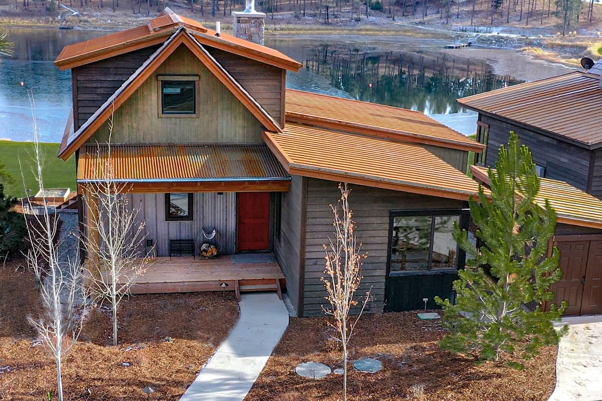 A two-story wooden cabin with a sloped roof, a front porch, and a view of a lake.