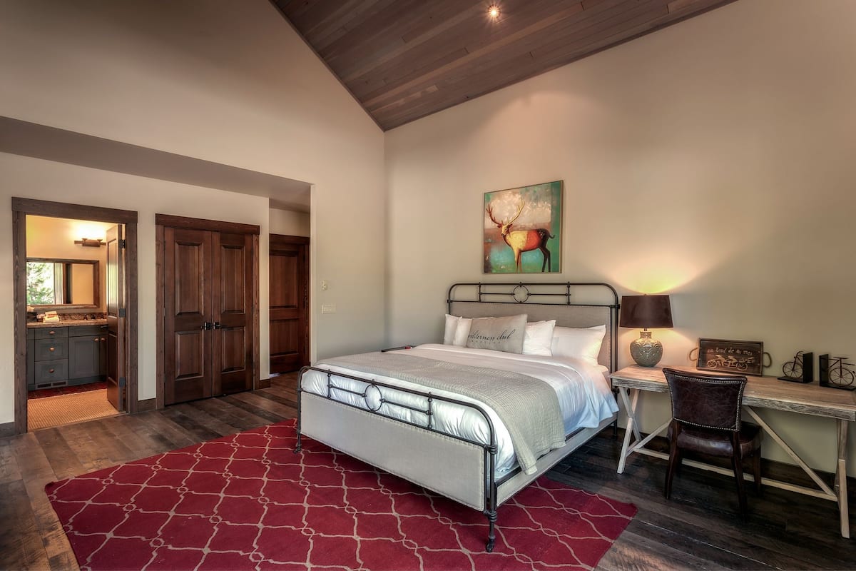 A bedroom with a bed, a desk, a chair, a lamp, and a painting on the wall.