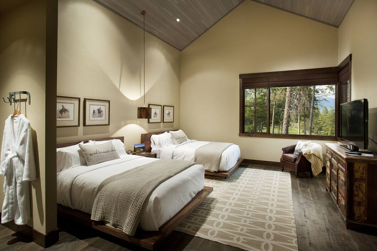 A bedroom with two beds, a television, and a window with a forest view.