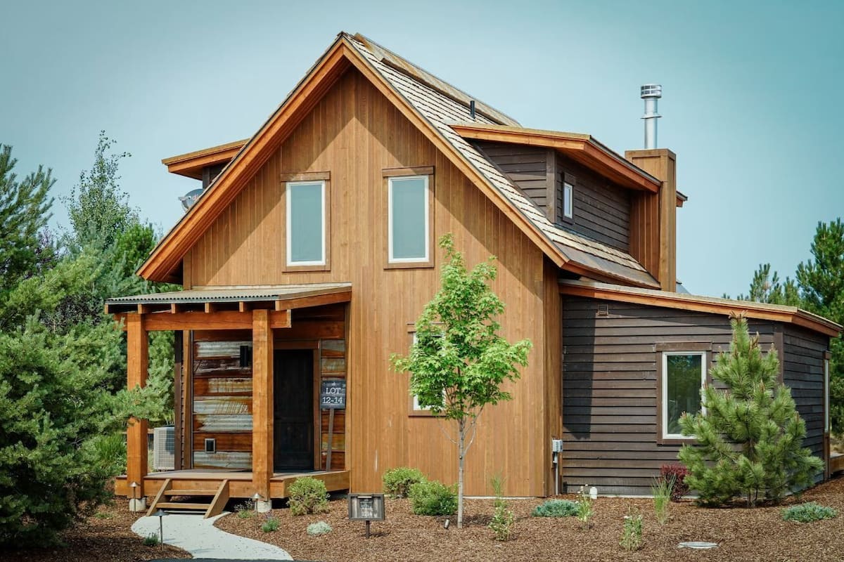 A modern wooden house with a prominent gable roof, large windows, and a chimney.