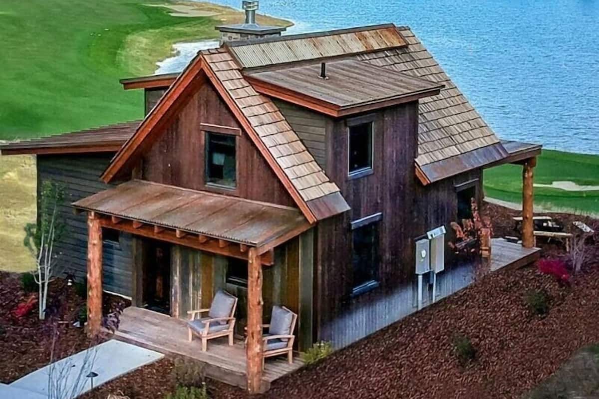 A rustic cabin with a porch and two chairs, overlooking a lake.