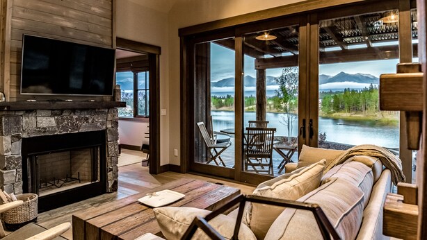 A cozy living room with a stone fireplace, a flat-screen TV, and a large window overlooking a lake and mountains. - Wilderness Club (Eureka)