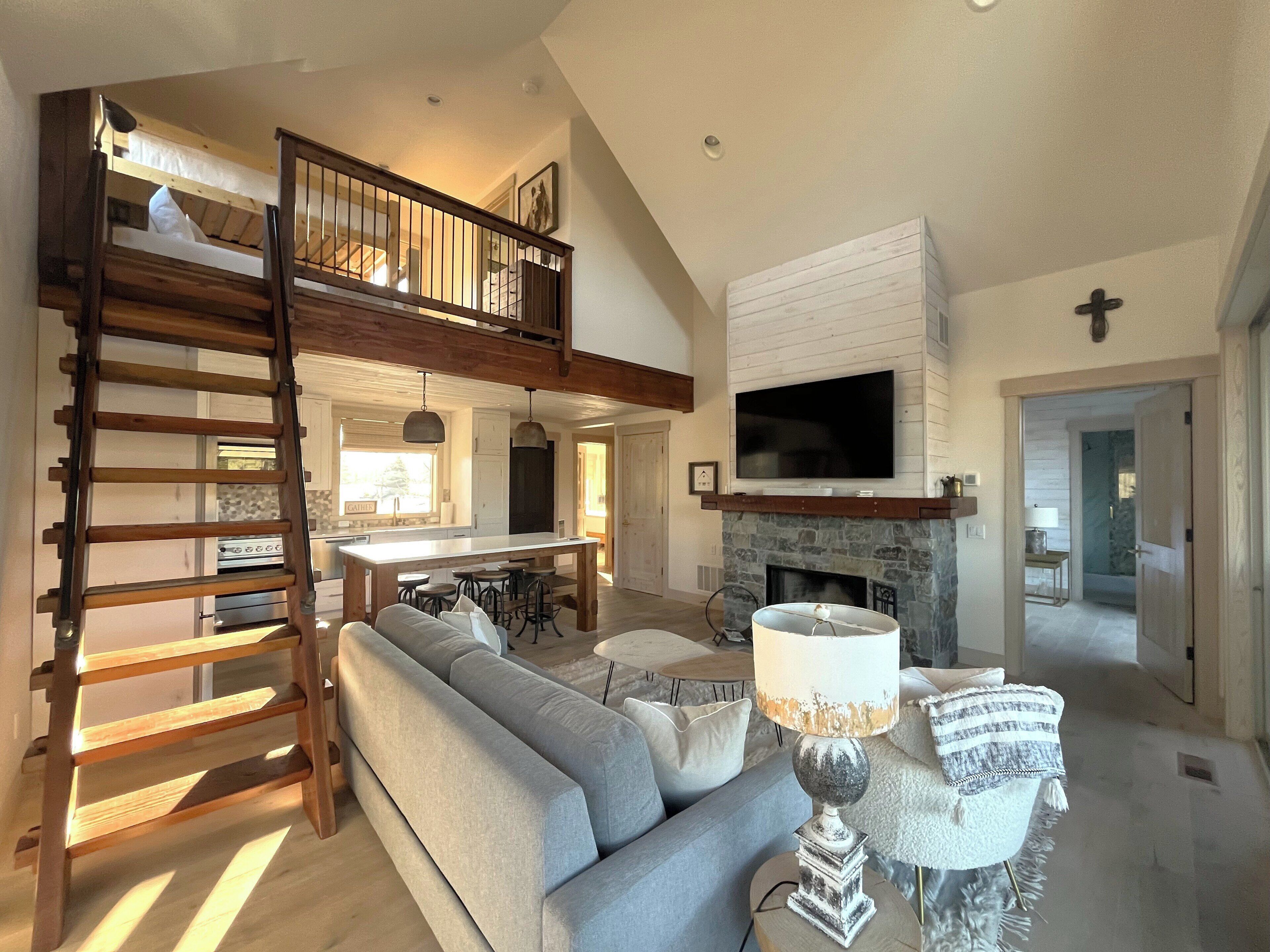 A spacious living area with a loft bedroom, a fireplace, a large TV, and a wooden ladder.
