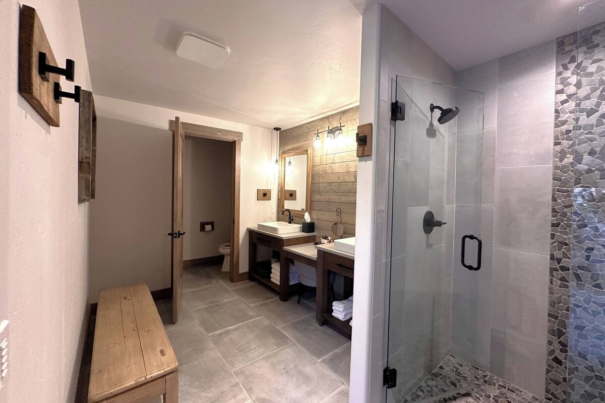 A modern bathroom with a glass shower enclosure, a wooden bench, and a vanity with a mirror.