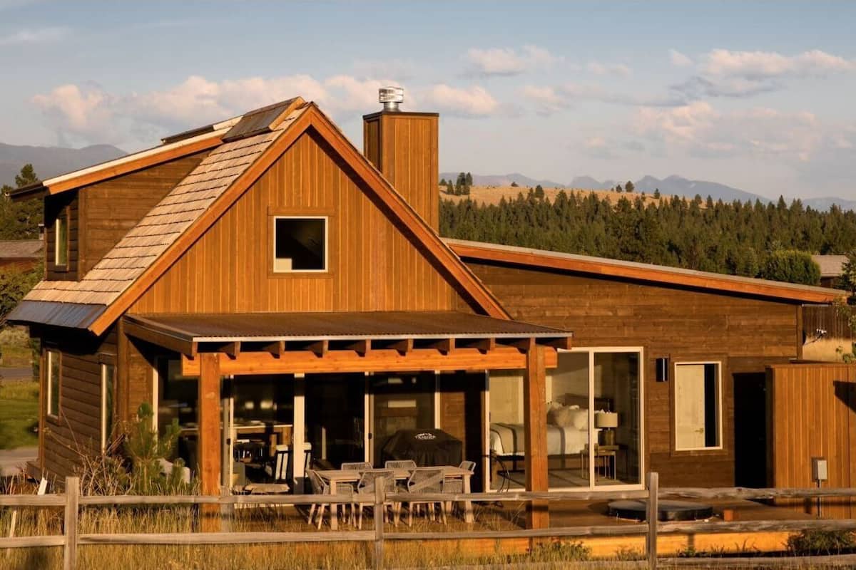 A wooden cabin with a sloped roof, large windows, and a patio area with outdoor furniture.