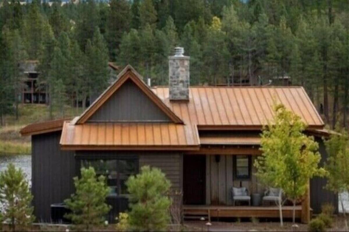A cabin with a wooden deck, a chimney, and a view of a forested area.