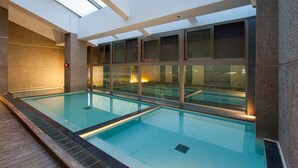 An indoor swimming pool with clear glass walls, a tiled floor, and a wooden deck area. - Luminous Hot Spring & Resort (Luye)