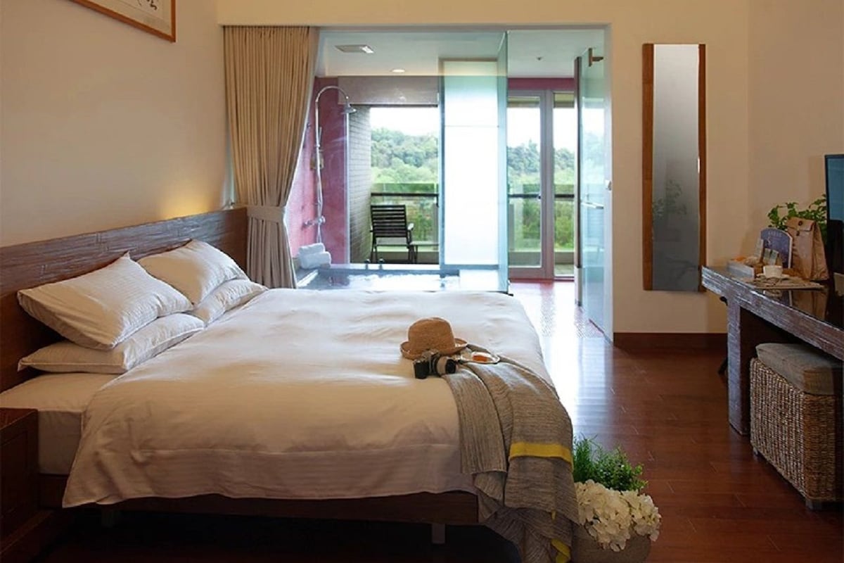 A hotel room with a large bed, a balcony with a chair, and a desk with a computer.