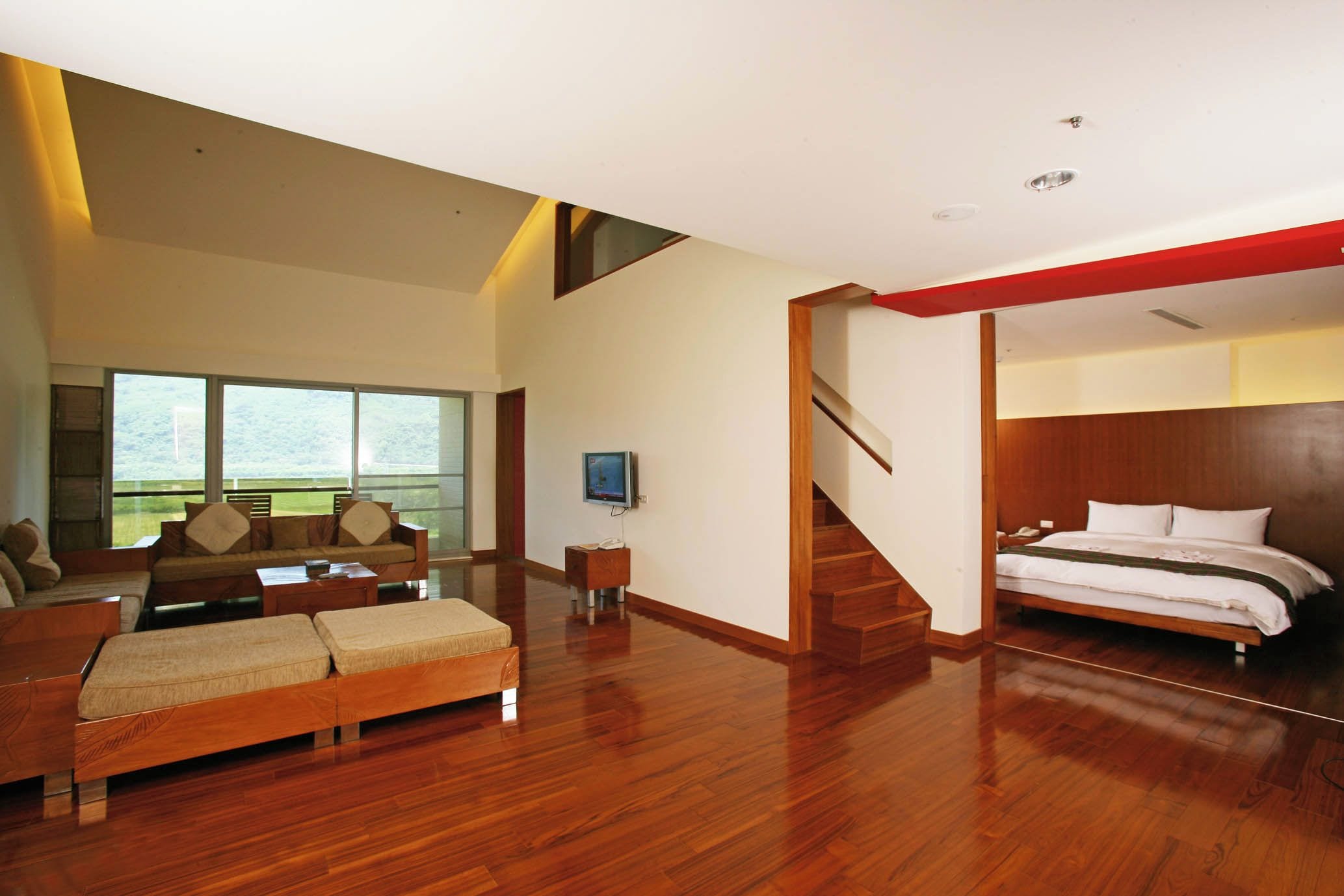 A modern hotel room with a wooden floor, a sofa, a bed, and a TV.