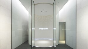 En modern hiss med glasväggar, minimalistisk design och en cirkelformad ljusinstallation i botten.