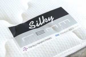 A hotel bed with a tag labeled "Silky" and "Hankyū Hanshin Hotels."