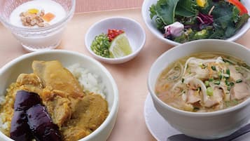 A table with four bowls of food, including rice with chicken, a soup with noodles, a salad, and a bowl of yogurt with fruit.
