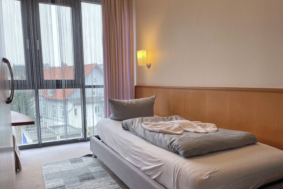 Une chambre d’hôtel avec un lit, une table de chevet, une lampe et une vue sur les bâtiments par la fenêtre.