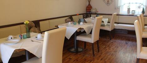 A dining area with tables set for four, wooden flooring, and a window with a view.