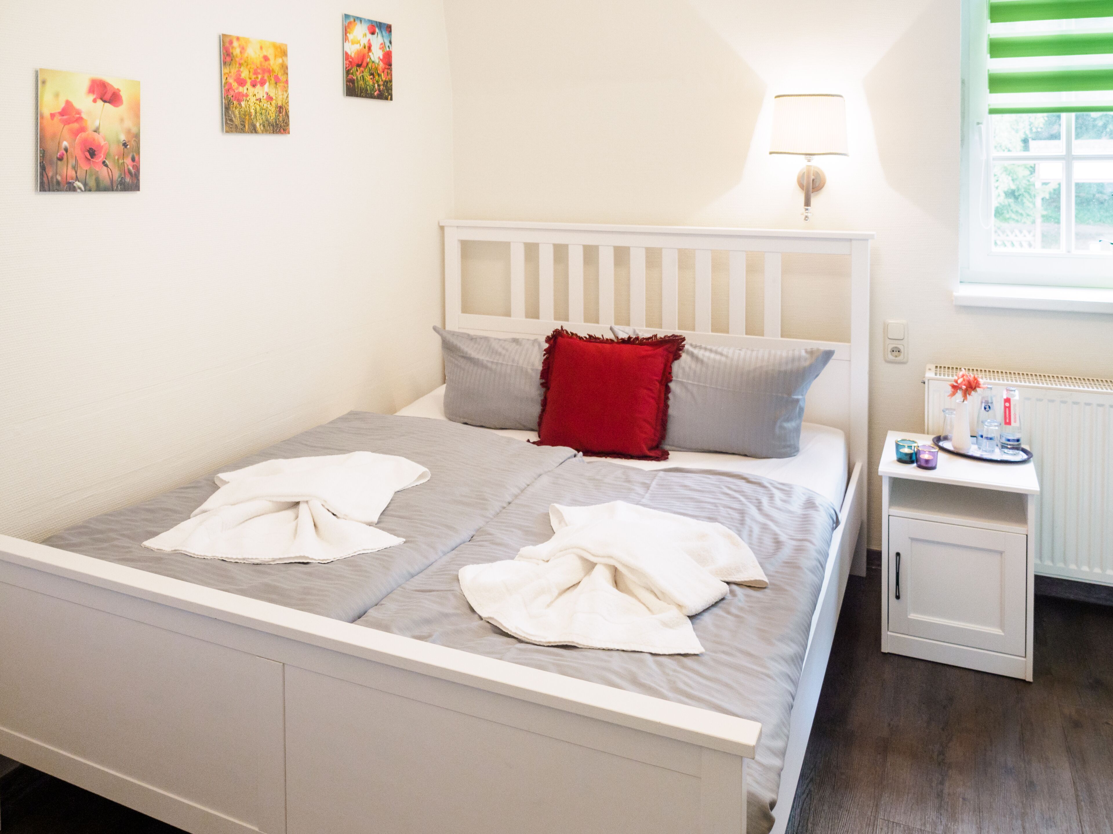 A neatly made bed with a white headboard, a bedside table with a lamp, and artwork on the wall.