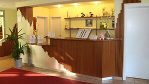 Zona de recepción con mostrador de madera, plantas en macetas y una pantalla mural.